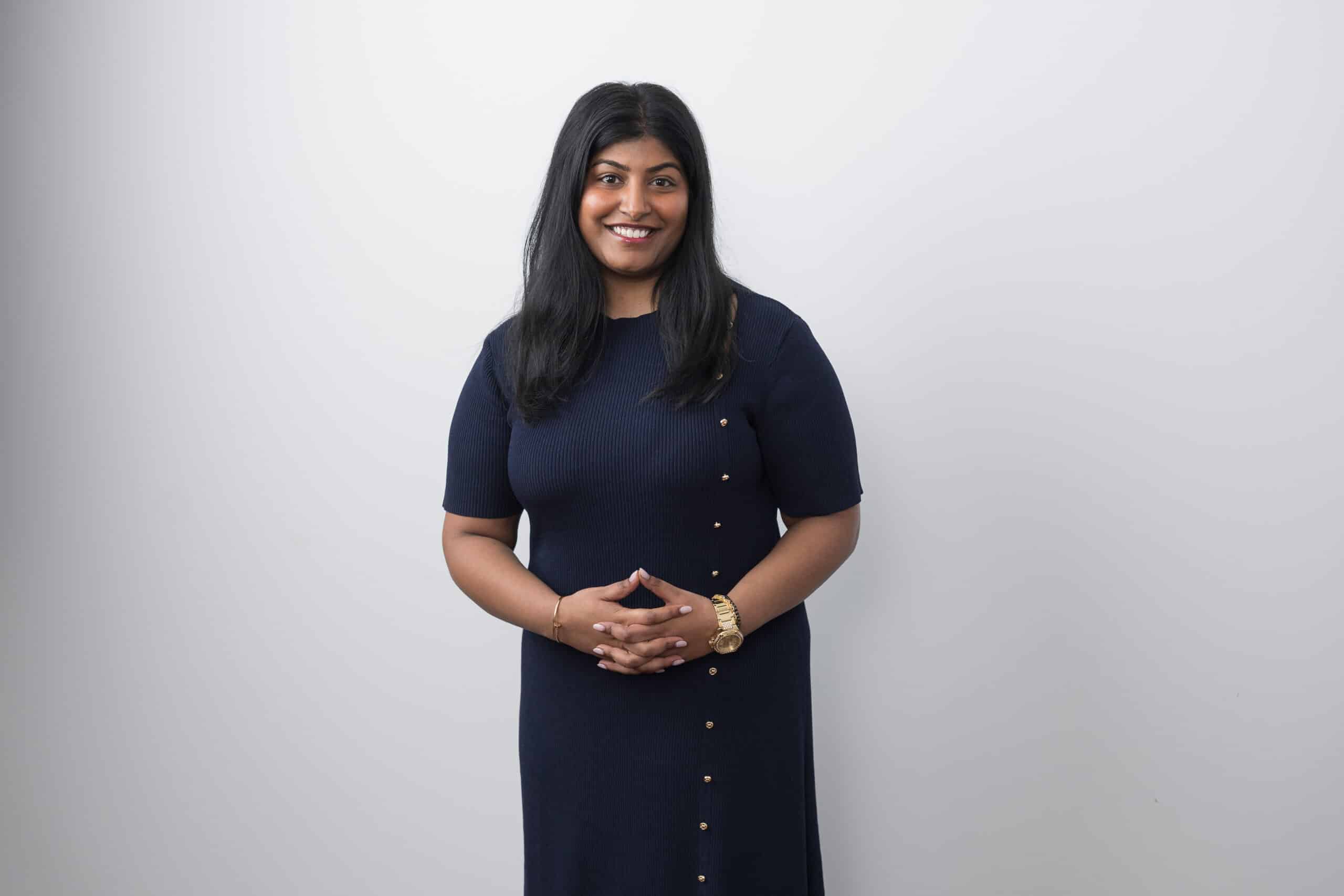 Woman in a navy buttoned dress standing against a pale studio backdrop.